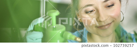 Close up portrait of relaxed young woman, female gardener smiling while spraying plants and taking care of her home garden 102739257