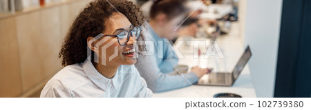 Smiling woman freelancer working laptop and making notes while sitting in cozy coworking 102739380