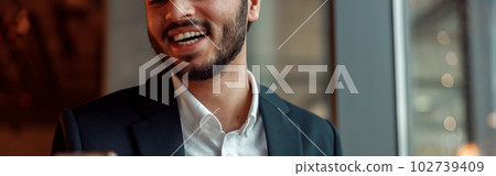 Smiling Indian businessman wearing suit is using phone during lunch time in cafe 102739409