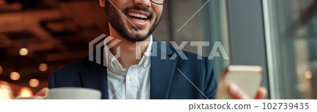 Smiling Indian businessman wearing suit is using phone during lunch time in cafe. Blurred background 102739435