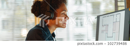 Smiling Afro american woman interior designer in headphones works in home office Smiling Afro american woman interior designer in headphones works in home office 102739486