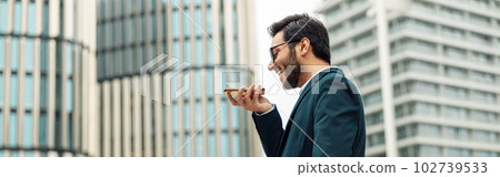 Indian Businessman with laptop recording audio message to client standing near office during break 102739533