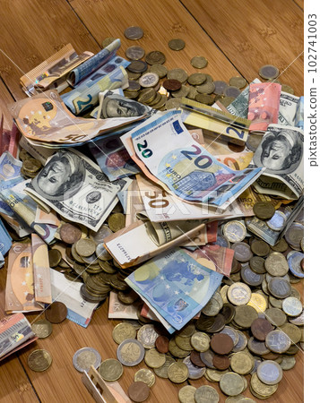Pile of coins and banknotes lies on a wooden floor Pile of coins and banknotes lies on a wooden floor 102741003