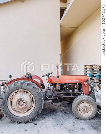 Small old rustic tractor stands near the wall of a building 102741176