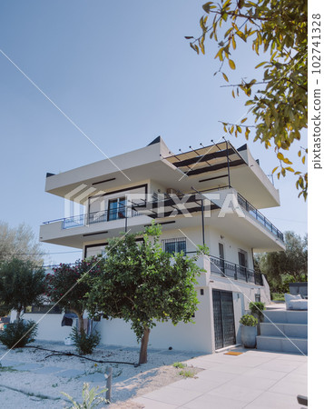Two-storey cottage with terraces in the garden against the blue sky Two-storey cottage with terraces in the garden against the blue sky 102741328