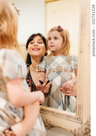a cute little girl in a plaid dress and mom looks in the mirror and primping. 102741526
