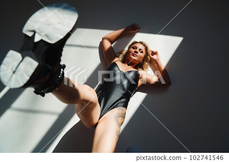 a bold and sexy blonde in a leather swimsuit and boots on the white floor a bold and sexy blonde in a leather swimsuit and boots on the white floor 102741546