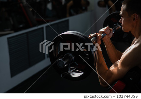 Man doing EZ barbell bicep exercises on Scott bench.  102744359