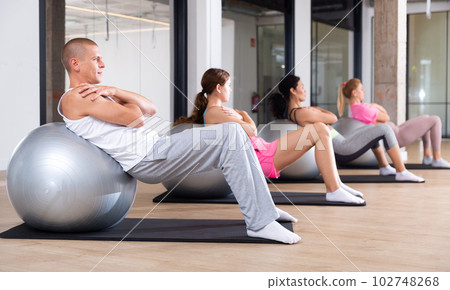 Sports people perform a back stretching exercise with a ball Sports people perform a back stretching exercise with a ball 102748268