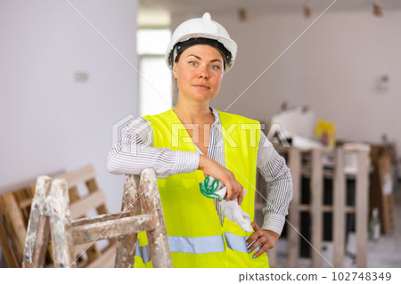 Female foreman in protective yellow vest and hard hat in renovated room Female foreman in protective yellow vest and hard hat in renovated room 102748349