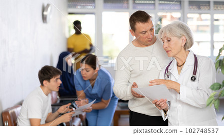 Elderly woman doctor gives document to adult man to sign Elderly woman doctor gives document to adult man to sign 102748537