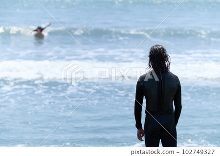 Back view of a surfer and a man watching the situation Back view of a surfer and a man watching the situation 102749327