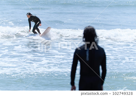 A woman surfing and a man watching A woman surfing and a man watching 102749328