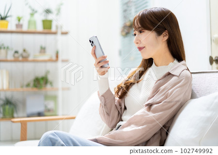 一個女人坐在沙發上,看著她的智能手機 一個女人坐在沙發上,看著她的智能手機 102749992
