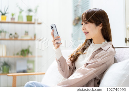 一個女人坐在沙發上,看著她的智能手機 一個女人坐在沙發上,看著她的智能手機 102749993