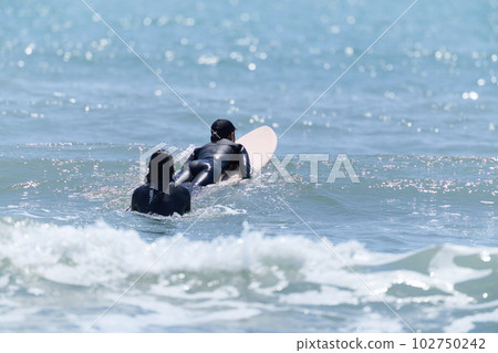 A woman surfing and a man watching 102750242