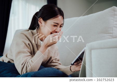 Happy young asian woman relax on comfortable couch at home texting messaging on smartphone Happy young asian woman relax on comfortable couch at home texting messaging on smartphone 102752023