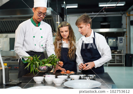 Chef teacher teaches cooking to the group children in class kitchen room Chef teacher teaches cooking to the group children in class kitchen room 102753612