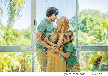 It's a boy. Expectant parents mother, father and their elder son are having a gender reveal party. A married the couple burst the balloon and the blue confetti flew out. Family, pregnancy and prenatal 102757235