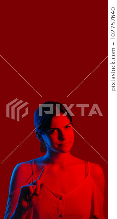 Warning woman. Prevention gesture. Strict confident neon color light girl showing finger up sign scolding isolated on dark red copy space background. Warning woman. Prevention gesture. Strict confident neon color light girl showing finger up sign scolding isolated on dark red copy space background. 102757640