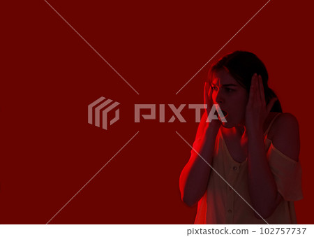 Terrified girl portrait. Intense fear feeling. Despair scared stressed neon color light woman frightened expression nervous breakdown isolated on dark red empty space background. 102757737