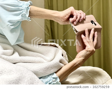 Elderly woman's hand looking at smartphone in bed Elderly woman's hand looking at smartphone in bed 102759259