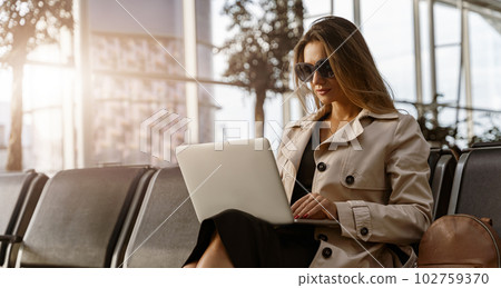 Young businesswoman in sunglasses with luggage in airport waiting room working laptop 102759370