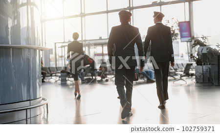 Two pilots walking along the airport terminal following the stewardess 102759371