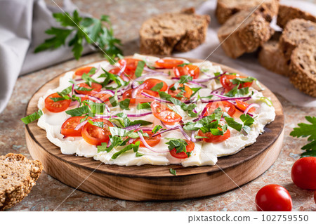 Homemade butter board with tomatoes, red onions and herbs and baguette pieces on the table Homemade butter board with tomatoes, red onions and herbs and baguette pieces on the table 102759550