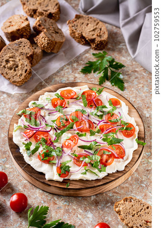 Trendy butter board with tomatoes, onions and parsley and slices of bread on the table vertical view 102759553