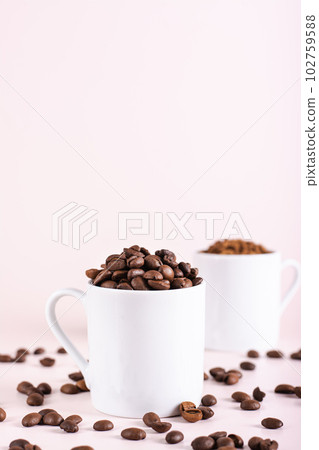 Roasted coffee beans and instant coffee in cups on pink background vertical view Roasted coffee beans and instant coffee in cups on pink background vertical view 102759588