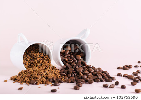 Dry instant coffee granules and roasted coffee beans are scattered from cups on the table Dry instant coffee granules and roasted coffee beans are scattered from cups on the table 102759596