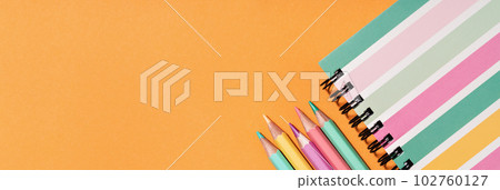 Colored pastel pencils and stripy notepad on orange. Back to School or drawing and creativity concept. Copy space. Top view banner Colored pastel pencils and stripy notepad on orange. Back to School or drawing and creativity concept. Copy space. Top view banner 102760127
