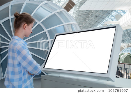Woman looking at interactive white touchscreen display kiosk at exhibition 102761997