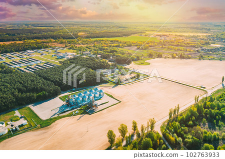 Aerial Elevated Top View Modern Granary, Grain-drying Complex, Commercial Grain Or Seed Silos In Sunny Spring Rural Landscape. Corn Dryer Silos, Inland Grain Terminal, Grain Elevators In A Field 102763933