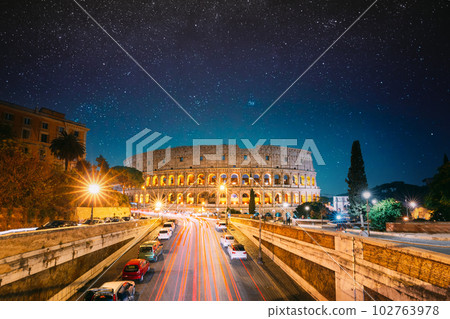 Rome, Italy. Colosseum Also Known As Flavian Amphitheatre In Evening Or Night Time. Night Traffic Light Trails Near Famous World Landmark. Bright Blue Night Sky. Amazing Night Starry Sky Background Rome, Italy. Colosseum Also Known As Flavian Amphitheatre In Evening Or Night Time. Night Traffic Light Trails Near Famous World Landmark. Bright Blue Night Sky. Amazing Night Starry Sky Background 102763978