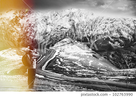 Stepantsminda, Gergeti, Georgia. Sunlit Man Tourist Traveler Photographer Taking Pictures Photos Of Amazing Georgian Mountain Landscape In Early Winter. Sun-drenched View. Black And White Photo 102763990