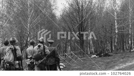 Group Of Re-enactors Dressed As Soviet Russian Soldiers Escort Civilians. Soviet Russian Soldiers Uniform. Evacuation Of Civilians. Black And White Video 102764026