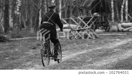 Re-enactor Dressed As Nkvd Forces Rides A Bike. Peoples Commissariat For Internal Affairs, Abbreviated Nkvd, Was Interior Ministry Of The Soviet Union. Black And White Video Re-enactor Dressed As Nkvd Forces Rides A Bike. Peoples Commissariat For Internal Affairs, Abbreviated Nkvd, Was Interior Ministry Of The Soviet Union. Black And White Video 102764031