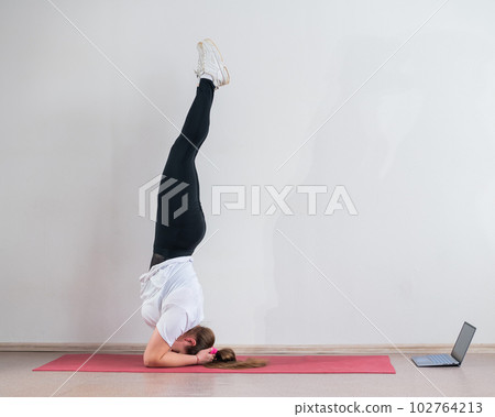 A chubby young woman watches an online yoga lesson on a laptop. Distance sports training. Forearm stand 102764213