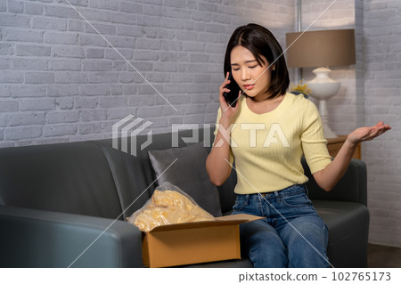 Young Asian woman complaining on mobile phone when she received a wrong or damaged parcel from ordering online. E-Commerce and online shopping mistake 102765173