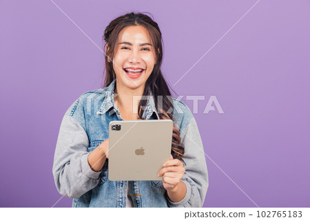 Portrait of Asian beautiful young woman smiling using tablet computer, Happy lifestyle female teen touching screen on digital tablet pc, studio shot isolated on purple background 102765183