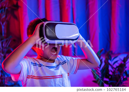 Asian little kid boy wearing virtual reality goggles experiencing reality, Child wear VR helmet excited open mouth at home dark purple and blue background, Virtual technology 102765184