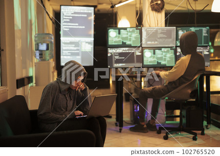 Two hackers working on computers to crack encryption late at night, working on phishing and cyberattack. Criminals committing cybercrime with anonymous code, hacking pc system. Two hackers working on computers to crack encryption late at night, working on phishing and cyberattack. Criminals committing cybercrime with anonymous code, hacking pc system. 102765520