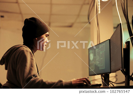 Asian man using computers to hack database information, cracking online passwords to steal data. Male thef using spyware and trojan virus to break into network server late at night. 102765547