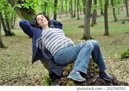 Pregnant woman relaxing on a tree trunk 102768561