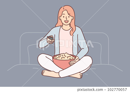Woman with TV remote turns on series sitting on bed in bedroom and holds cup of popcorn Woman with TV remote turns on series sitting on bed in bedroom and holds cup of popcorn 102770057