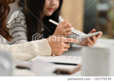 Cropped image of little girl using digital tablet, doing school assignment with mother at desk 102770556