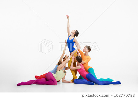 Elegant young girls, ballet dancers in multicolored bright clothes making creative performance, dancing against grey studio background. 102770788