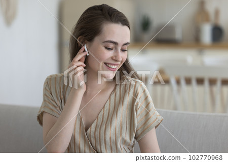 Positive happy pretty girl touching small white earbud in ear Positive happy pretty girl touching small white earbud in ear 102770968